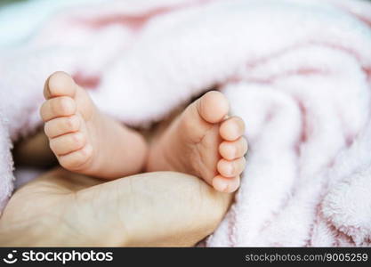 Newborn baby feet on the mother’s hand on a white blanket.