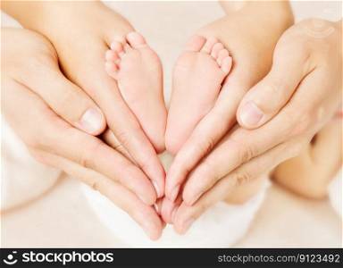 Newborn baby feet parents holding in hands. Love simbol as heart sign.