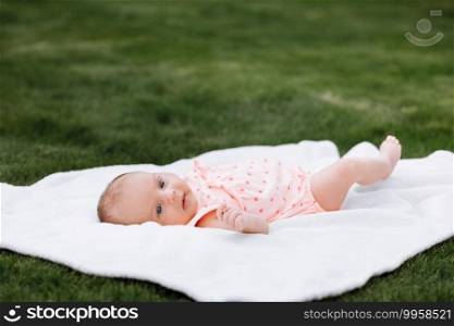 Newborn baby girl on grass in the park outdoors, lies on a white blanket looking around. selective focus. Newborn baby girl on grass in the park outdoors, lies on a white blanket looking around. selective focus.