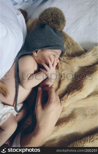 Newborn baby girl sleeping lying on a blanket on the bed next to her mother’s hand. Baby sleeping on a blanket with her mother’s hand