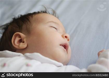 Newborn baby girl sleeping on blue sheets at home