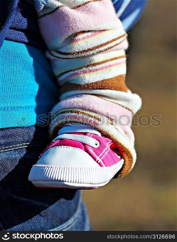 Newborn baby leg in the pink shoe, in the sling with mother