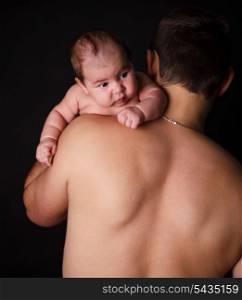 Newborn baby on father&rsquo;s shoulder on black