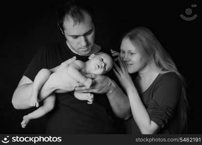 Newborn baby on the father&#39;s hands and mother on black