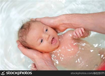 Newborn baby swimming in bath with help of father&rsquo;s hands