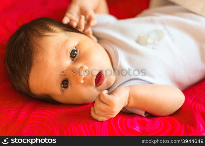 Newborn boy looks surprised with his mouth open on a red background.