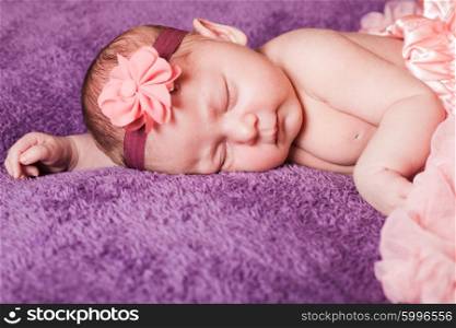 Newborn pretty baby girl in pink tutu dress sleeps on the purple textile. The newborn girl