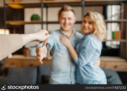 Newly married love couple receive as a gift the keys to the apartment. Happy lifestyle, beautiful relationship. Smiling husband and wife takes a present