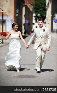 Newly wed couple run on sidewalk