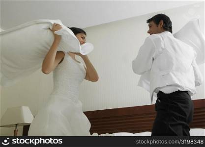Newlywed couple having a pillow fight on the bed