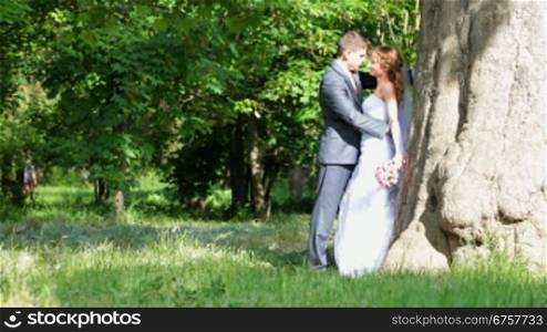 newlyweds are embracing in the park by a tree