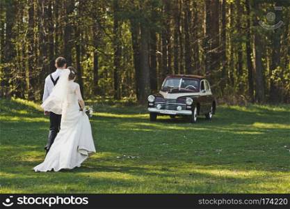 Newlyweds go to the car.. The couple walking toward a vintage car 3941.