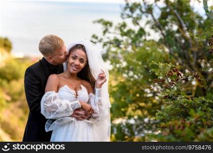 Newlyweds hug against the backdrop of a beautiful landscape, the guy kisses the girl who is looking into the frame