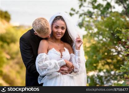 Newlyweds hug against the backdrop of a beautiful landscape, the guy kisses the neck of the girl who is looking into the frame