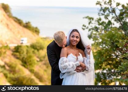 Newlyweds hug against the backdrop of a beautiful landscape, the guy kisses the shoulder of the girl who shyly looks up