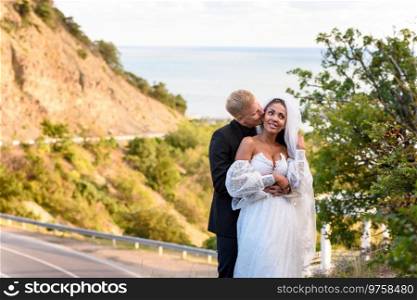 Newlyweds hugging against the backdrop of a beautiful mountain landscape, the guy kisses the girl
