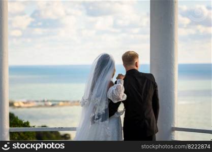 Newlyweds in a beautiful gazebo look into the distance at the sea