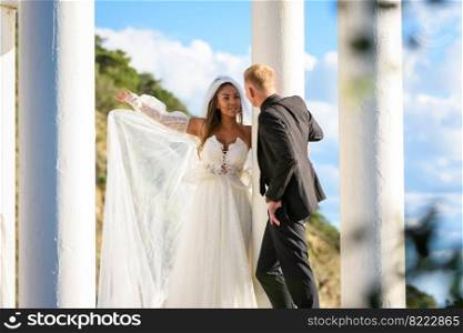 Newlyweds in a beautiful gazebo with columns against the backdrop of mountains and sky