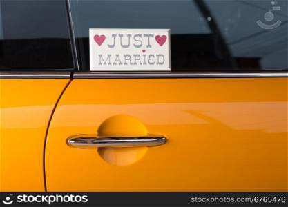 Newlyweds in his orange car to travel on honeymoon