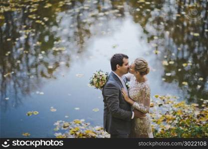 Newlyweds kissing on the background of a lake with autumn leaves.. A kiss on the background of the autumn pond 80.