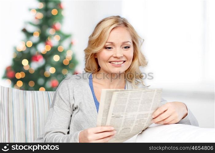 news, press, media, holidays and people concept - smiling woman reading newspaper at home over christmas tree lights background