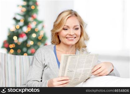 news, press, media, holidays and people concept - smiling woman reading newspaper at home over christmas tree lights background