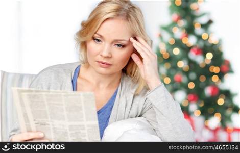 news, press, media, holidays and people concept - woman reading newspaper at home over christmas tree lights background