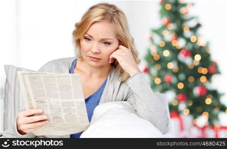 news, press, media, holidays and people concept - woman reading newspaper at home over christmas tree lights background