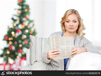 news, press, media, holidays and people concept - woman reading newspaper at home over christmas tree background