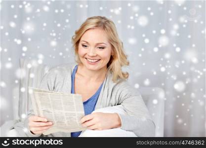 news, press, media, leisure and people concept - smiling woman reading newspaper at home over snow