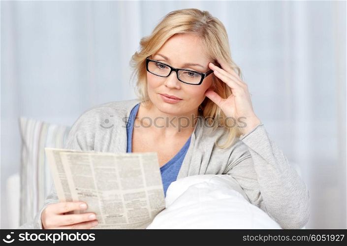 news, press, media, leisure and people concept - woman in eyeglasses reading newspaper at home