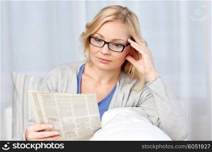 news, press, media, leisure and people concept - woman in eyeglasses reading newspaper at home