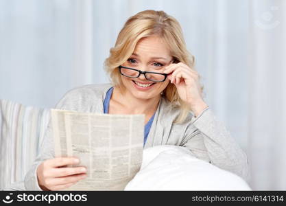 news, press, media, leisure and people concept - woman in eyeglasses reading newspaper at home