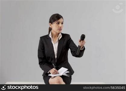 News reporter asking comment while writing in notepad against colored background