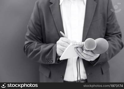 News reporter at press conference or media event, holding microphone, writing notes