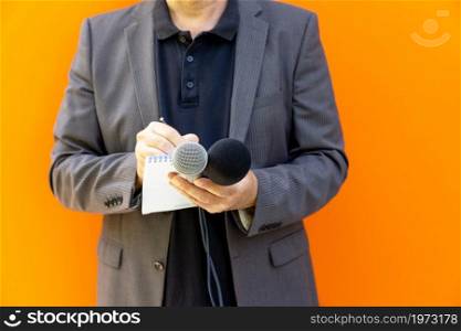 News reporter or broadcast journalist at press conference or media event, holding microphone, taking notes