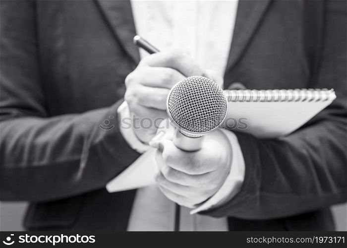 News reporter or TV journalist at press conference or media event, holding microphone and writing notes. Broadcast journalism concept.