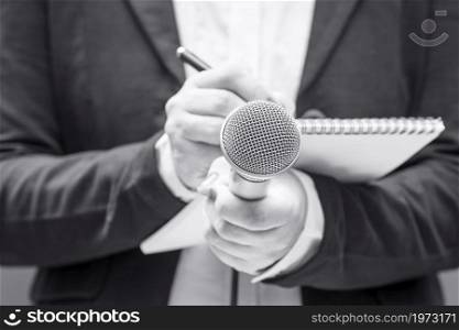 News reporter or TV journalist at press conference or media event, holding microphone and writing notes. Broadcast journalism concept.