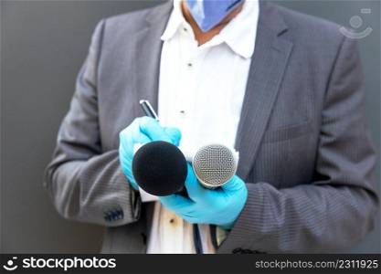 News reporter wearing protective gloves and face mask against coronavirus COVID-19 disease holding microphone reporting during virus pandemic
