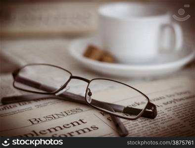 Newspapers and coffee cup, with reading glasses. Shallow depth of field. Focus on the word Business.