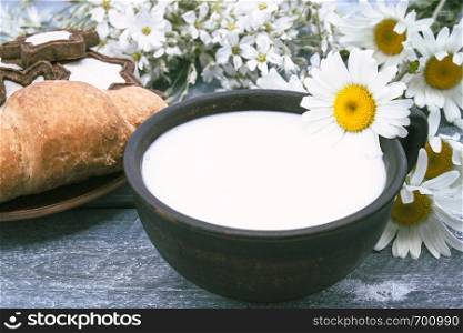 Next to the croissants and white chamomile flowers is a cup of milk.. Next to the croissants and daisies is a cup of milk.