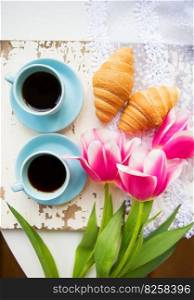 nice cup of coffee, croissants and pink tulips on old white table, close-up.. nice cup of coffee, croissants and pink tulips on old white table, close-up
