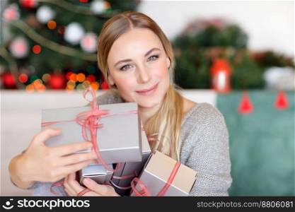 Nice female enjoying Christmas gifts, in anticipation of the opening of all the gift boxes, spending winter holidays at home with beautiful decorated Xmas tree. Woman enjoying Christmas gifts