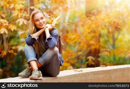 Nice female in bright sunny day sitting in the park and enjoying beautiful autumn nature and wonderful weather, with pleasure spending weekend outdoors