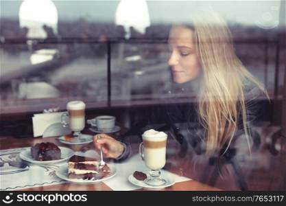Nice female in cafe eating cake and drinking latte in warm cozy atmosphere, enjoying sweet tasty dessert, casual urban life of young people