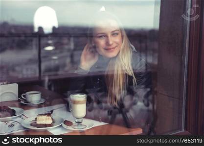 Nice female in cafe in warm cozy atmosphere, enjoying view through the window, casual urban life of young people