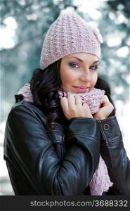 nice girl in winter dress with leather jacket and pink scarf and hat in a park