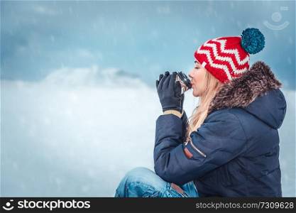 Nice girl sitting outside on a snowy winter day, warmed by hot tea, enjoying peaceful wintertime vacation
