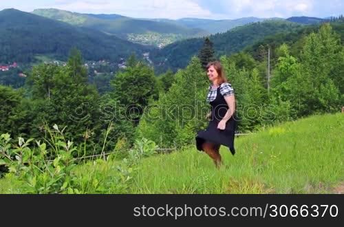 nice happy woman dances on top of hill among beautiful mountains