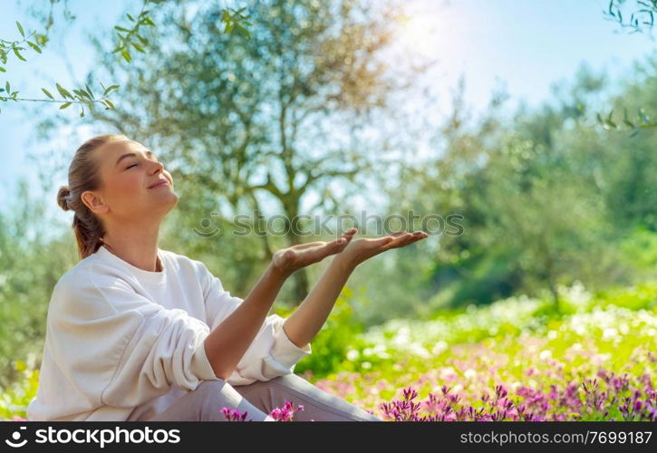 Nice happy woman sitting on flowers meadow in the garden, enjoying bright spring sunshine, active spring holidays in countryside